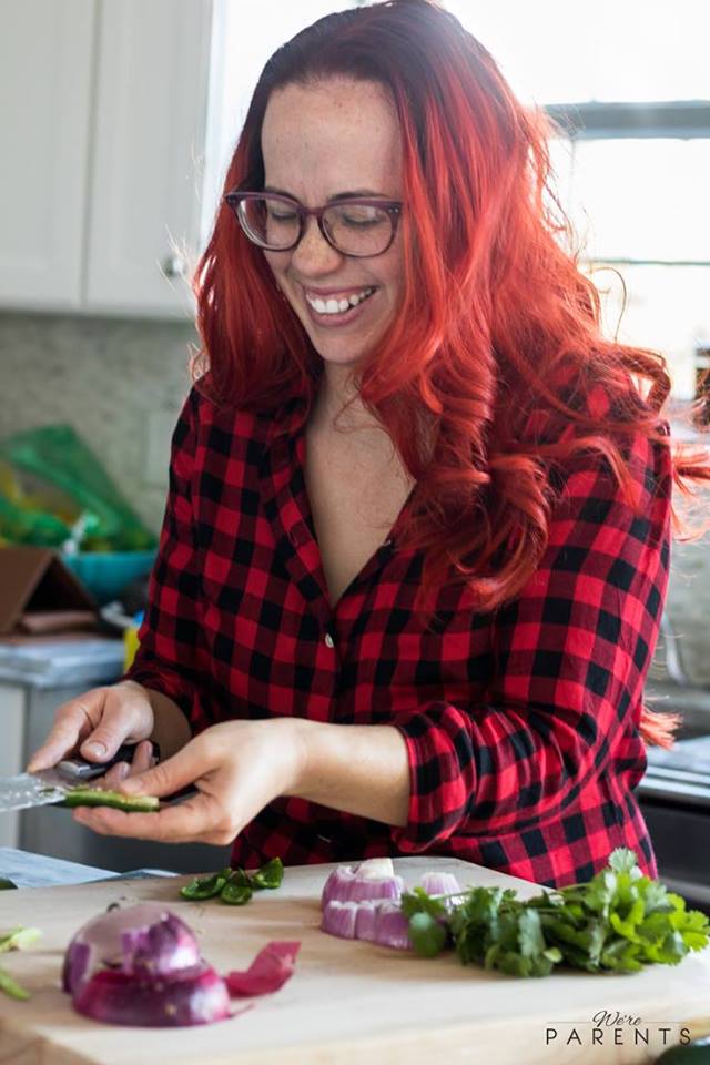 A woman laughing in the kitchen cutting an avocado.