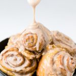 a black bowl of dairy free pumpkin cinnamon rolls with glaze drizzling from the top.