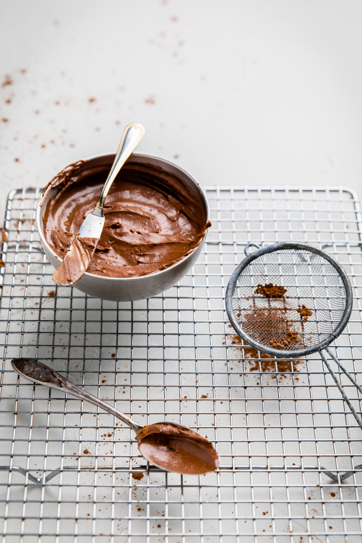 a bowl of dairy free chocolate frosting and a sieve of cocoa powder.