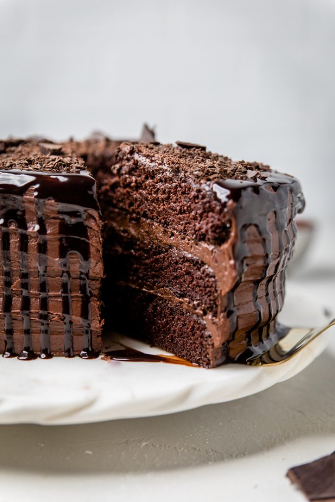 A slice of layered Vegan Chocolate cake with chocolate frosting being removed.