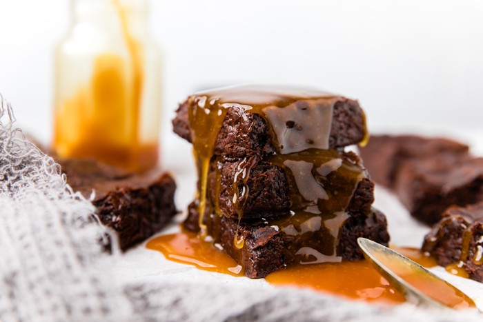 Fudgy dairy free brownies stacked on top of each other with caramel drizzle all over. 