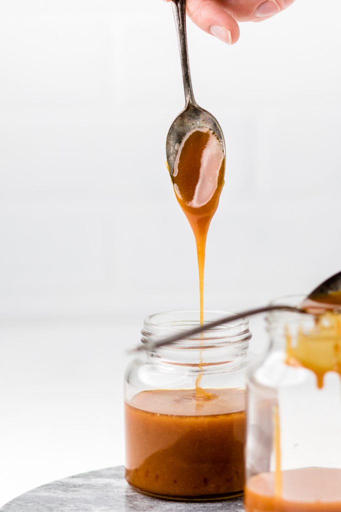 vegan caramel sauce dripping from a spoon into a jar.
