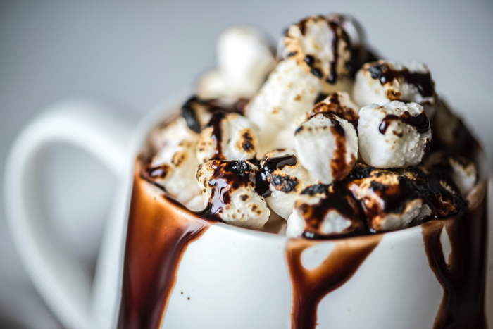 a white mug with hot chocolate drizzling out topped with toasted mini marshmallows.