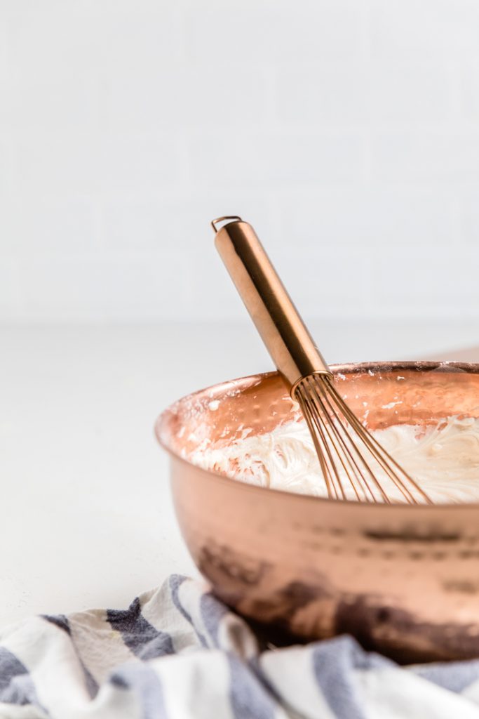 a bronze bowl and whisk with dairy free buttercream frosting.