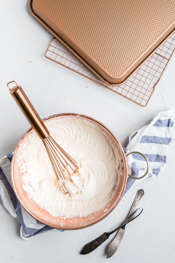 a bronze bowl and whisk with dairy free buttercream frosting.