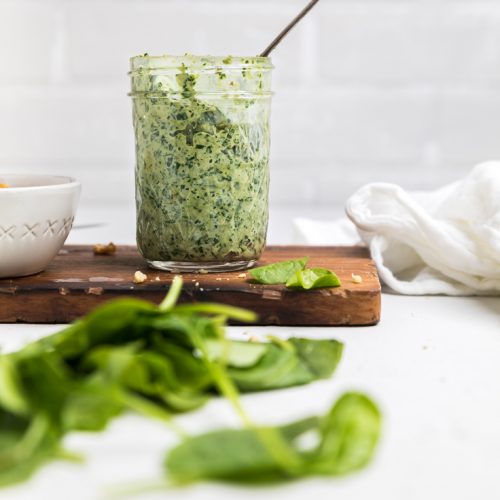 a jar of vegan pesto on a wooden board.