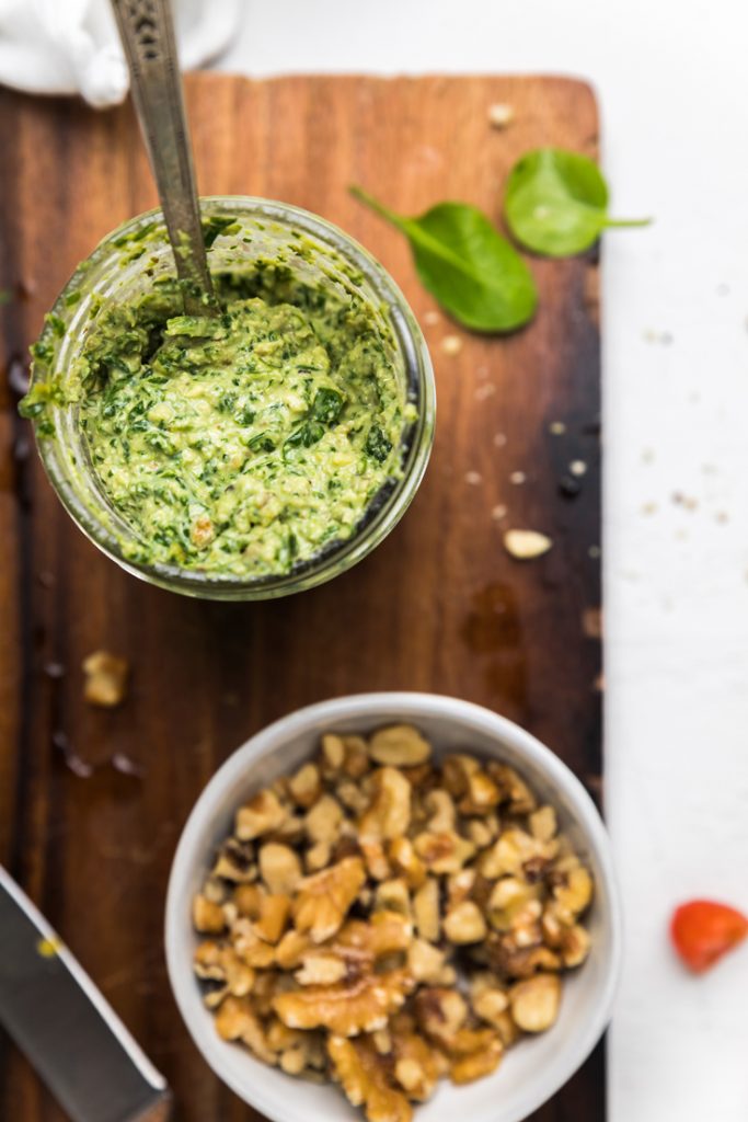 a jar of dairy free pesto and a bowl of walnuts on a wooden board.