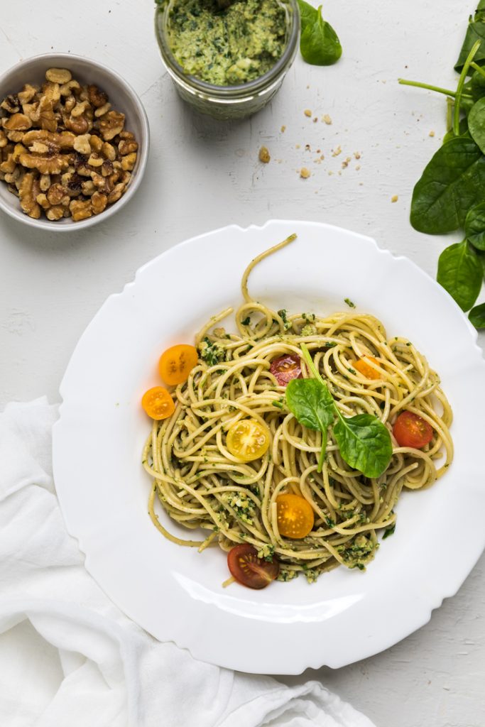 a plate of pasta with dairy free pesto topped with colorful tomatoes and basil.