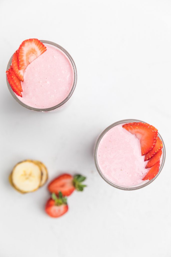 top of two glasses of dairy free strawberry banana smoothies with fresh strawberry slices.