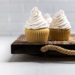 set of three dairy free vanilla cupcakes on a wooden board.