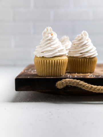 set of three dairy free vanilla cupcakes on a wooden board.