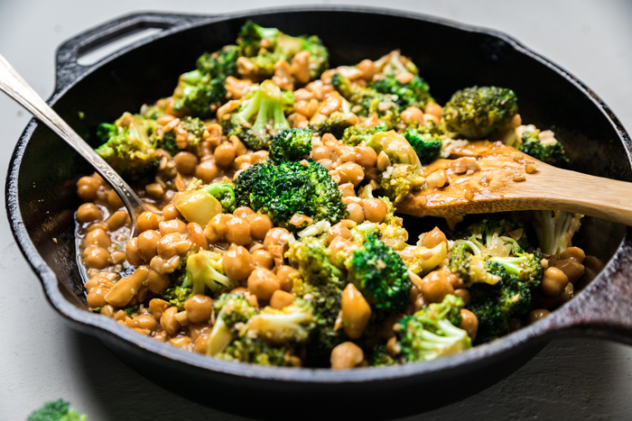 a spoon inside a skillet with vegan broccoli cashews and chickpeas and garlic sauce.
