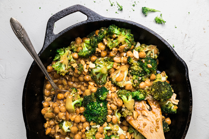 a wooden spoon in a skillet of vegan broccoli cashews and chickpeas with garlic sauce.