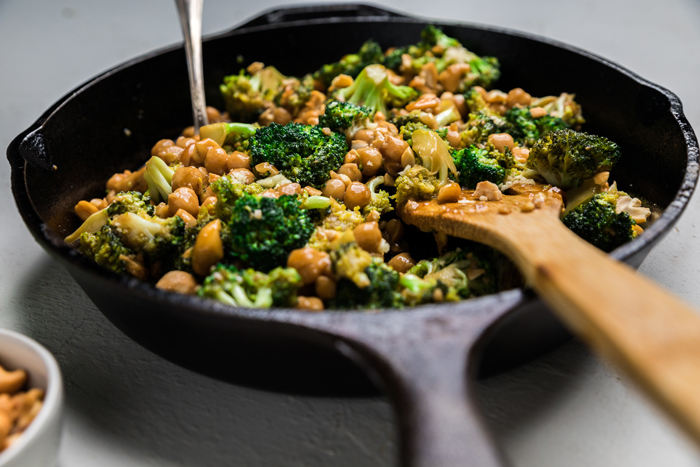 a skillet with broccoli cashews and chickpeas and garlic sauce.