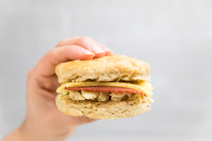 a hand holding a dairy free bacon egg and cheese biscuit sandwich.