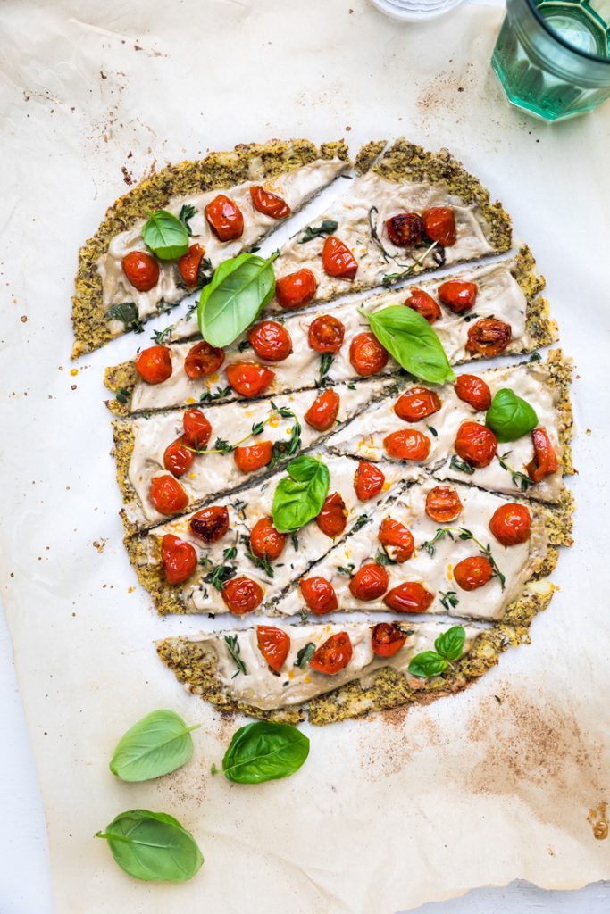 a dairy free cauliflower crust pizza with fresh basil, tomatoes, and cream sauce.