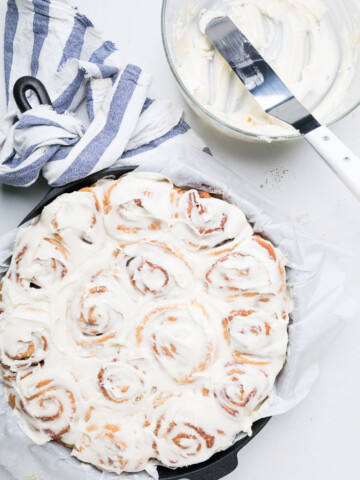 Dairy free cinnamon rolls with icing next to a bowl of icing.