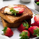 two slices of dairy free french toast on a plate with butter pats and fresh strawberries.