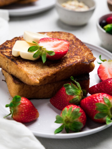 two slices of dairy free french toast on a plate with butter pats and fresh strawberries.