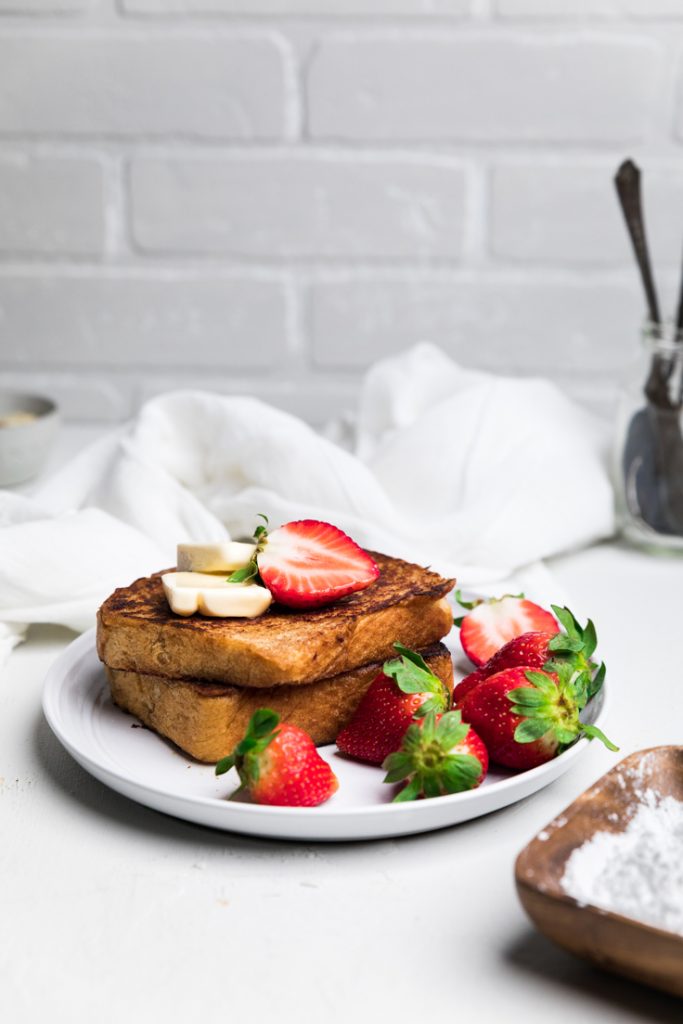 a plate with two slices of dairy free french toast with butter pats and fresh strawberries.