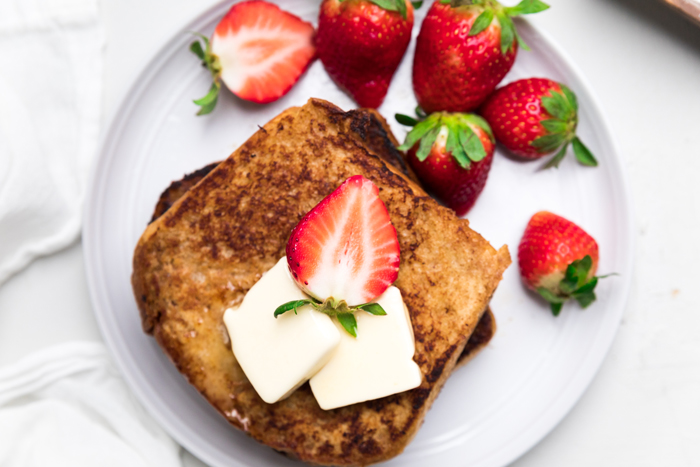 a slice of dairy free french toast on a plate with butter pats and fresh strawberries.