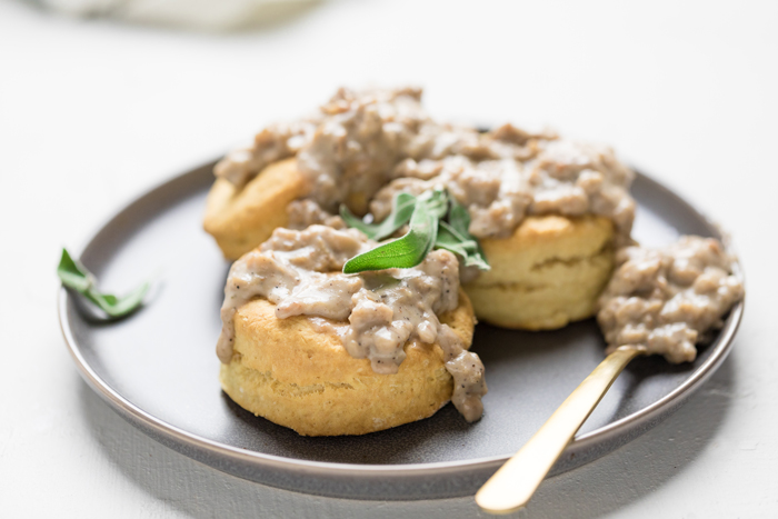 a plate of vegan sausage biscuits and gravy topped with fresh sage.