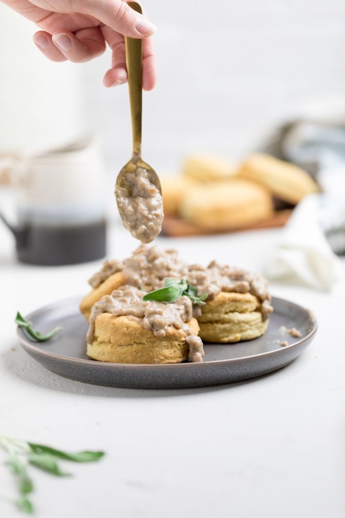 A spoon drizzling sausage gravy over vegan sausage biscuits and gravy.