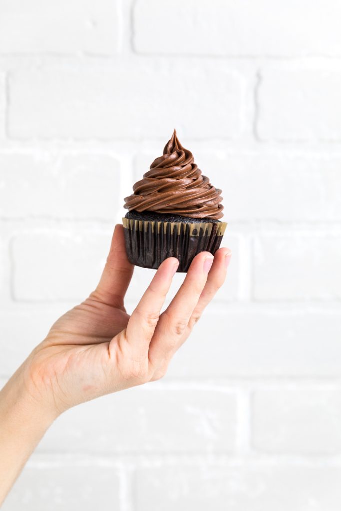 a hand holding a single dairy free chocolate cupcake.