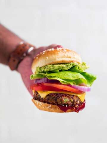 a hand holding a vegan black bean burger with fresh toppings.