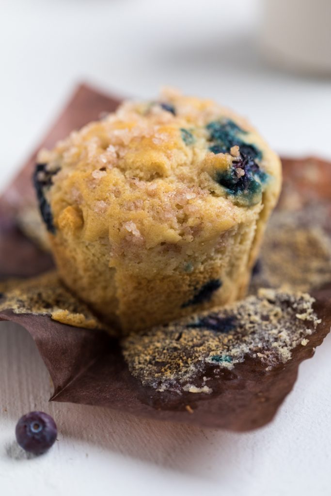 A single fluffy vegan blueberry muffins on a brown muffin liner.