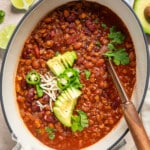 vegan apple chili in a pot topped with herbs, avocado, and jalapeno slices.
