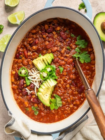 vegan apple chili in a pot topped with herbs, avocado, and jalapeno slices.