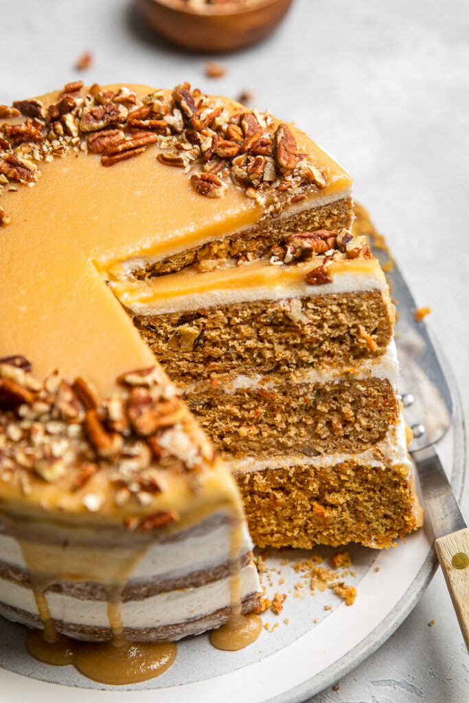 A slice of triple layered vegan carrot cake sliced with cream cheese and caramel frosting.