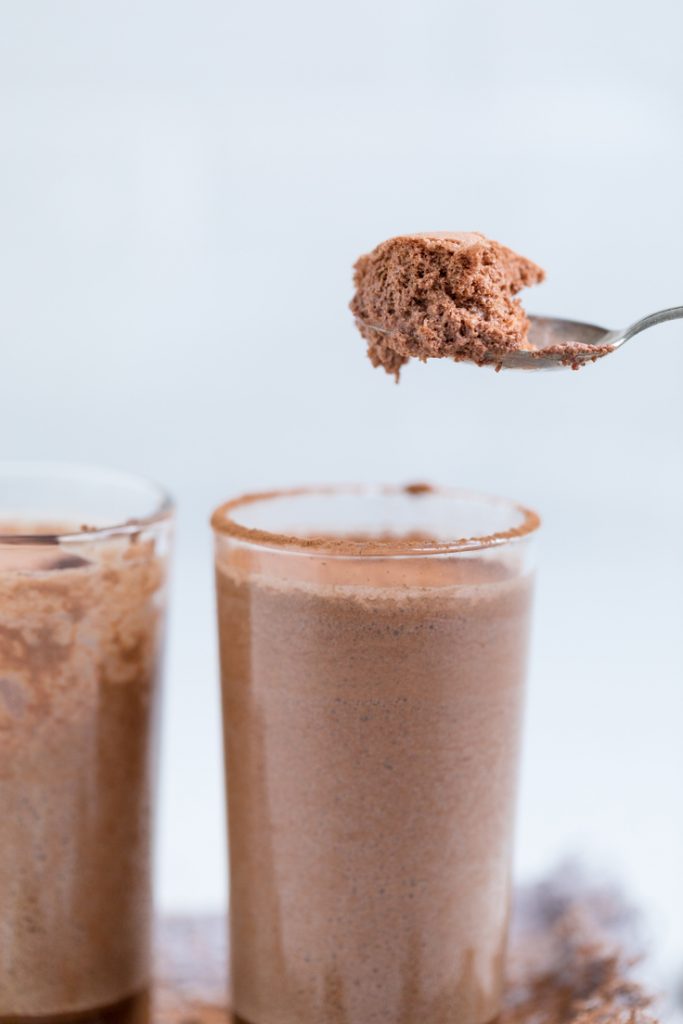 a spoon holding vegan chocolate mousse over a glass of mousse.