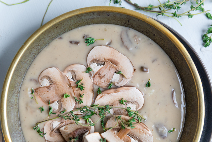 a bowl of vegan cream of mushroom soup with fresh thyme and mushroom slices.