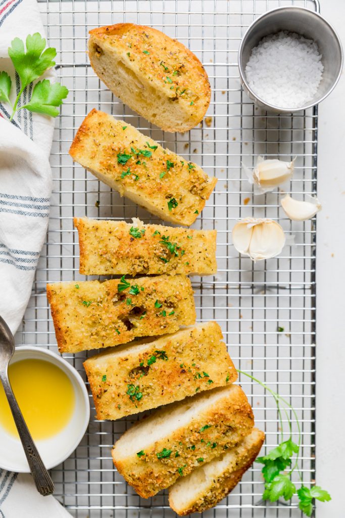 Loaf of vegan garlic bread cut into slices on a wire rack with bowl of melted butter.
