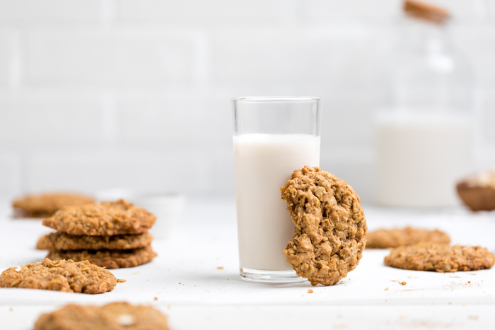 a vegan oatmeal cookie resting against a glass of non-dairy milk.