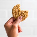 a hand holding a vegan oatmeal cookie with a bite taken out.