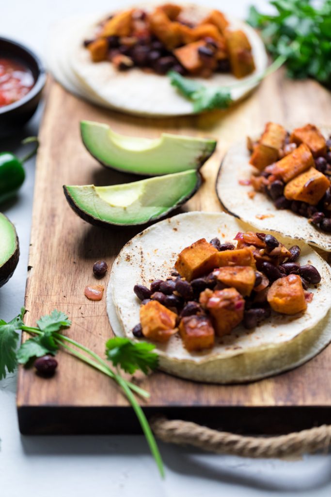 a wooden tray with vegan sweet potato and black bean tacos.