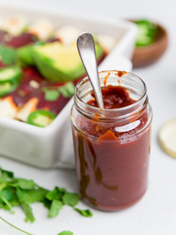 a jar with a silver spoon in it of a red enchilada sauce.