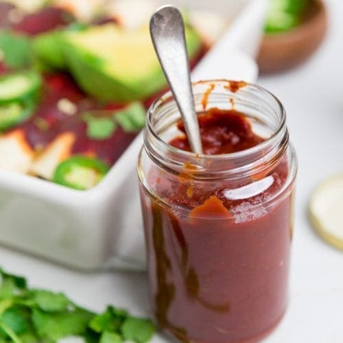 a jar with a silver spoon in it of a red enchilada sauce.