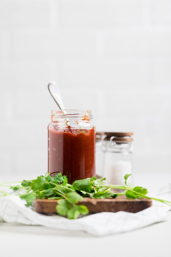 a glass jar of red enchilada sauce on a wooden board.