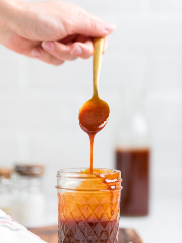 a hand holding a spoon of homemade vegan bbq sauce over a jar.