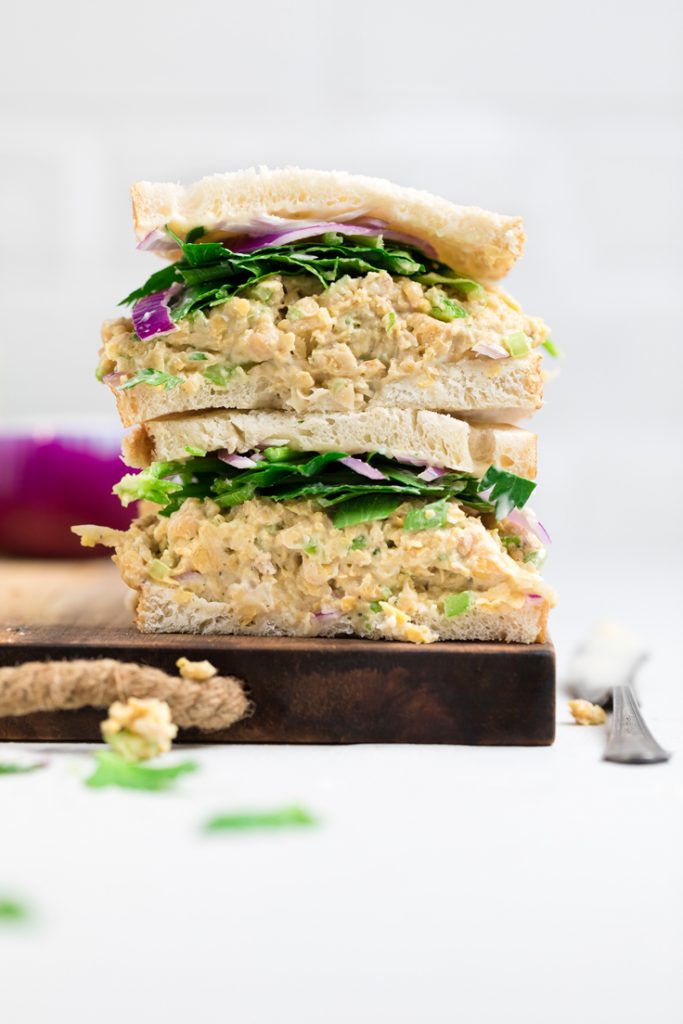 Easy chicken salad sandwich with lettuce and red onions halved and stacked on top of another.