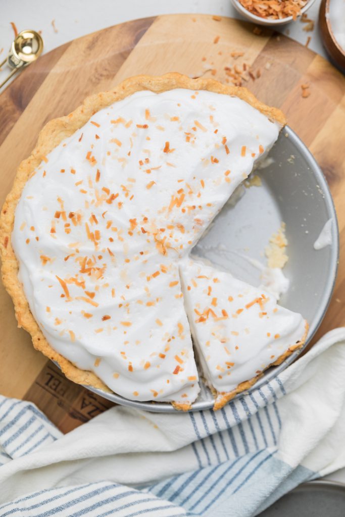 vegan coconut cream pie in a pie dish with a piece removed.