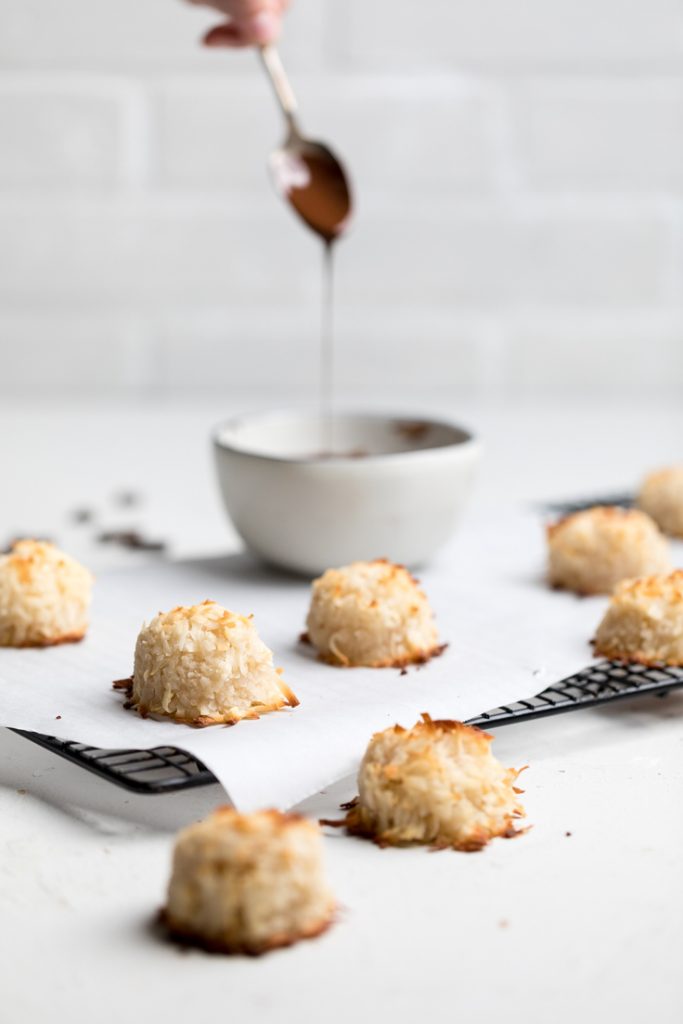 a batch of vegan coconut macaroons with a bowl of melted chocolate.