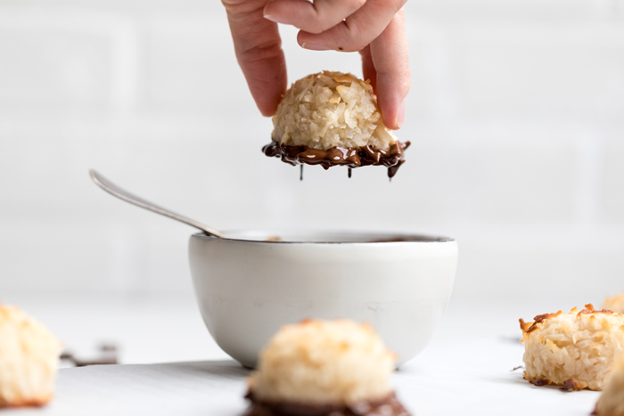 a hand dipping a vegan coconut macaroon in melted chocolate.