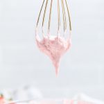 a gold whisk upside down with Vegan strawberry buttercream frosting.