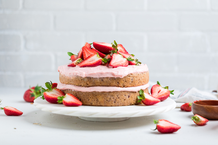 a double layered vegan strawberry cake on a white marble cake stand.
