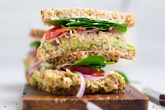 Chickpea Vegan tuna salad sandwich with tomato spinach and red onions halved and stacked.